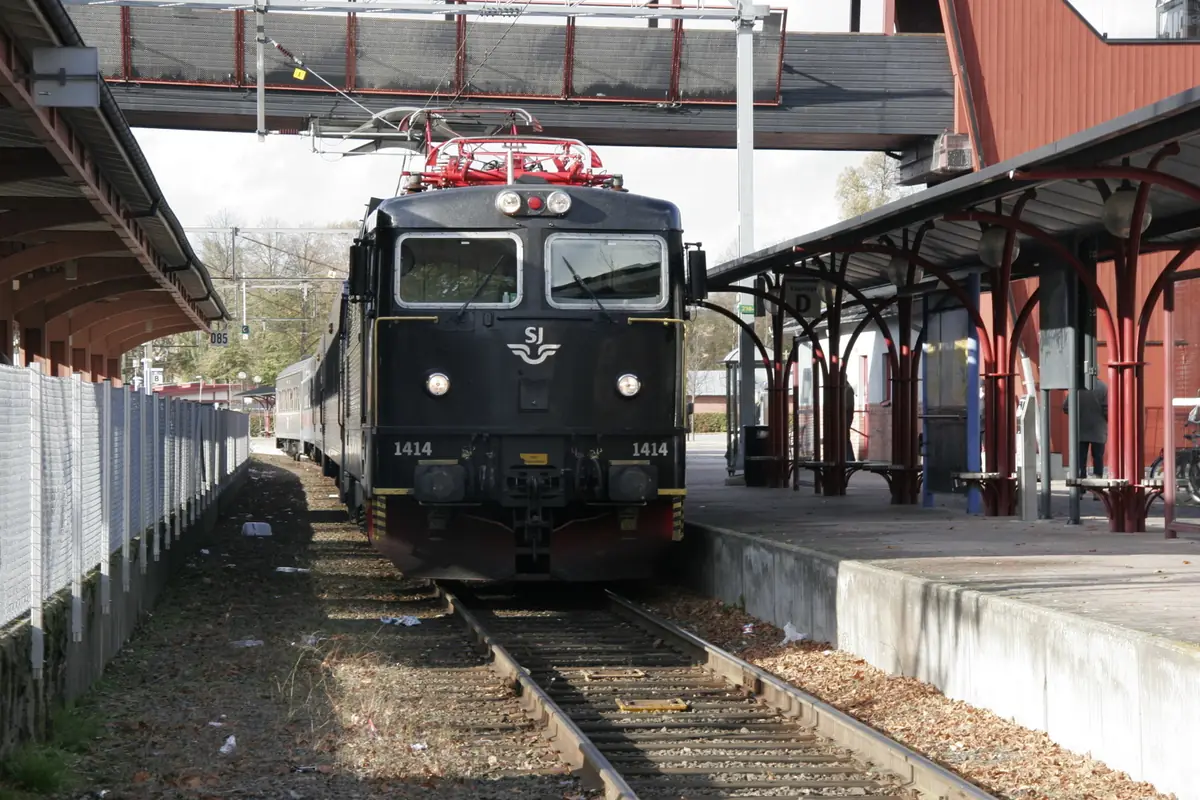 Ett svart elektriskt lok vid en perrong på en svensk järnvägsstation